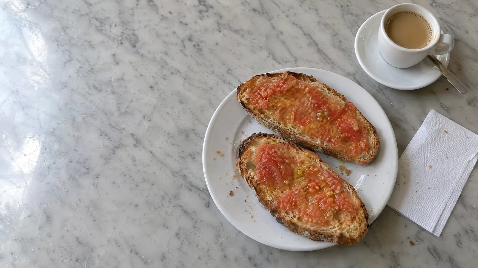 Una mesa con un cuaderno, un boligrafo, un vaso de agua y un desayuno a medias.